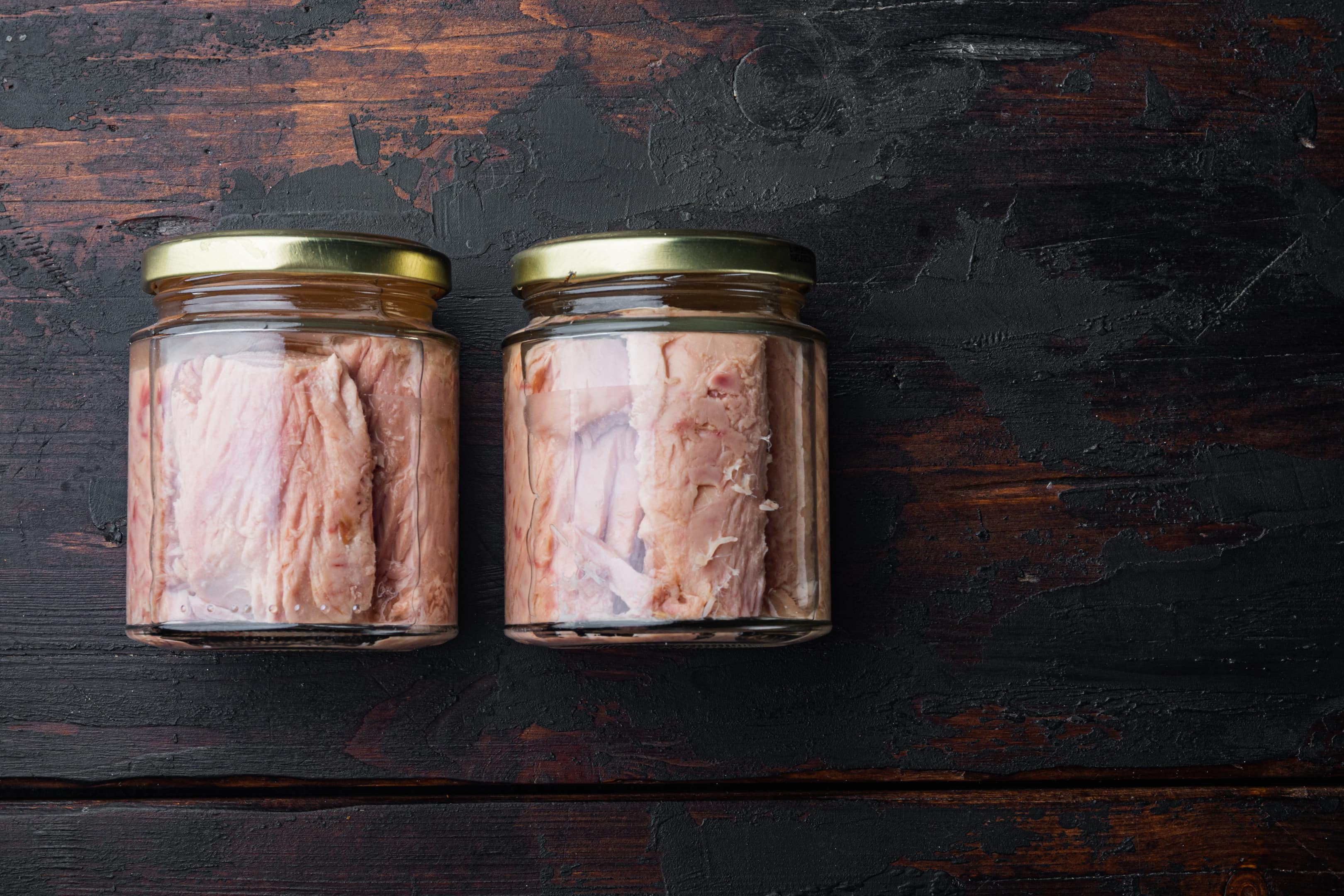 Jars of tuna fillet in olive oil on old wooden table