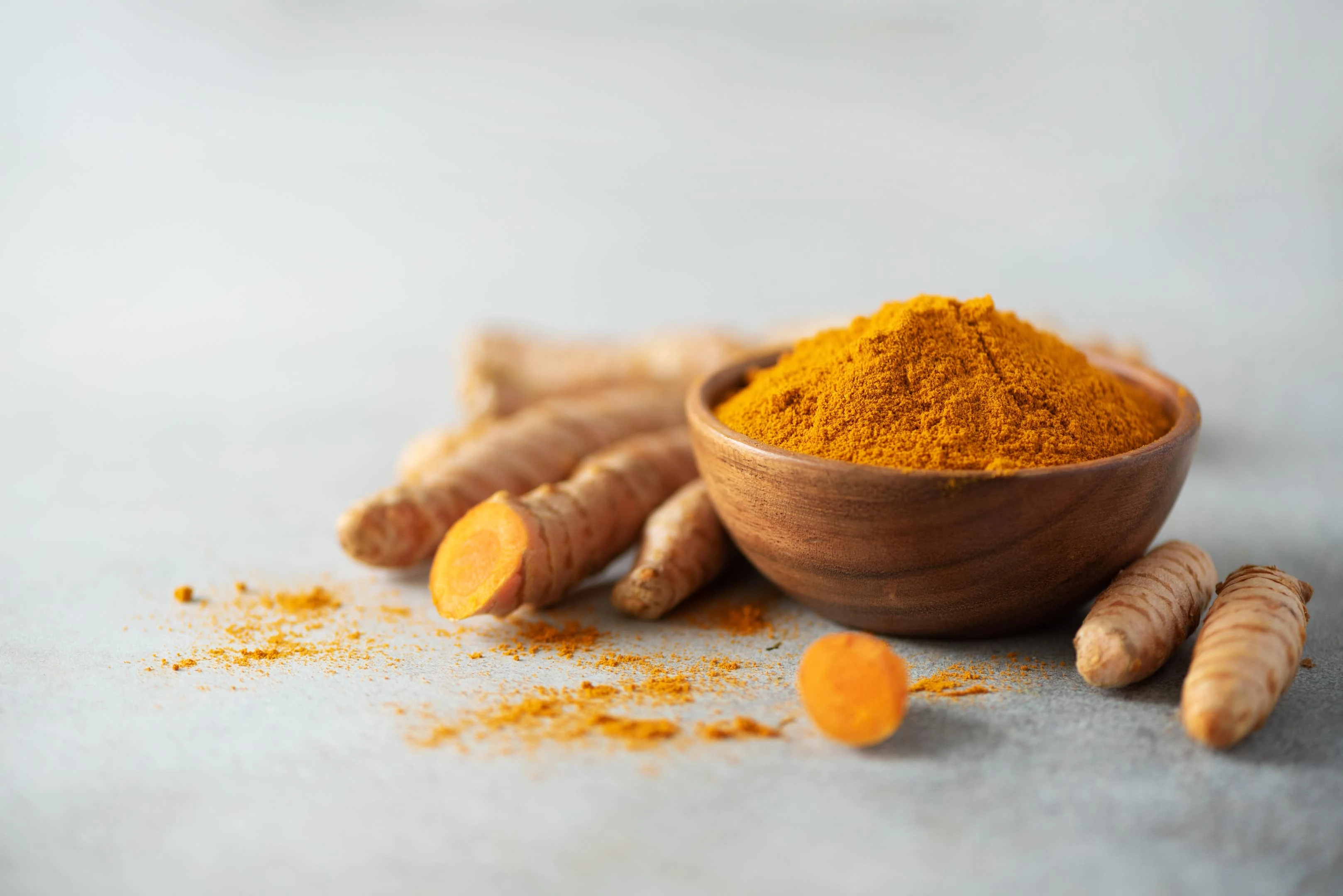 Turmeric powder in wooden bowl and fresh turmeric root on grey concrete background