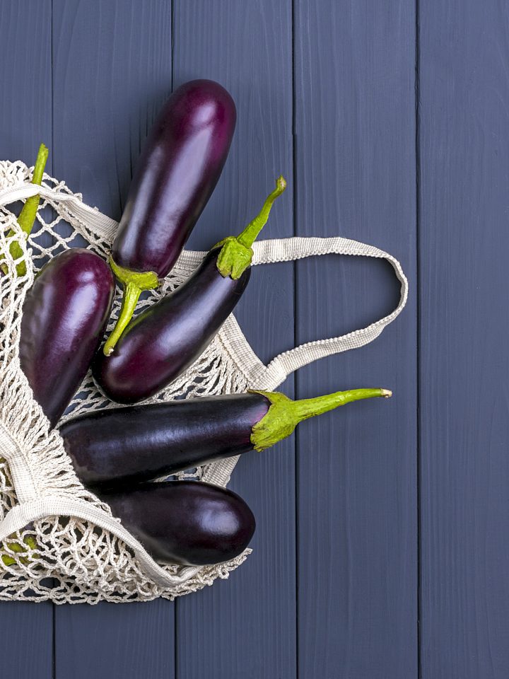 Eggplants in eco friendly mesh shopping bag on grey wooden table