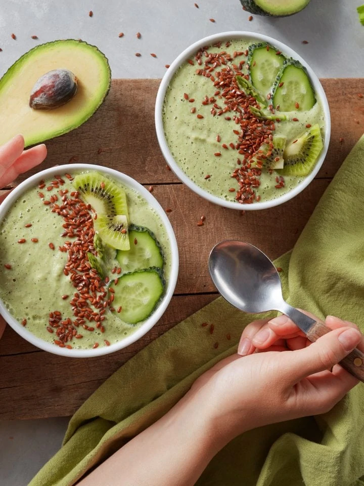 Green smoothie in bowls with fresh kiwi flaxseeds cucumber avocado with female hands