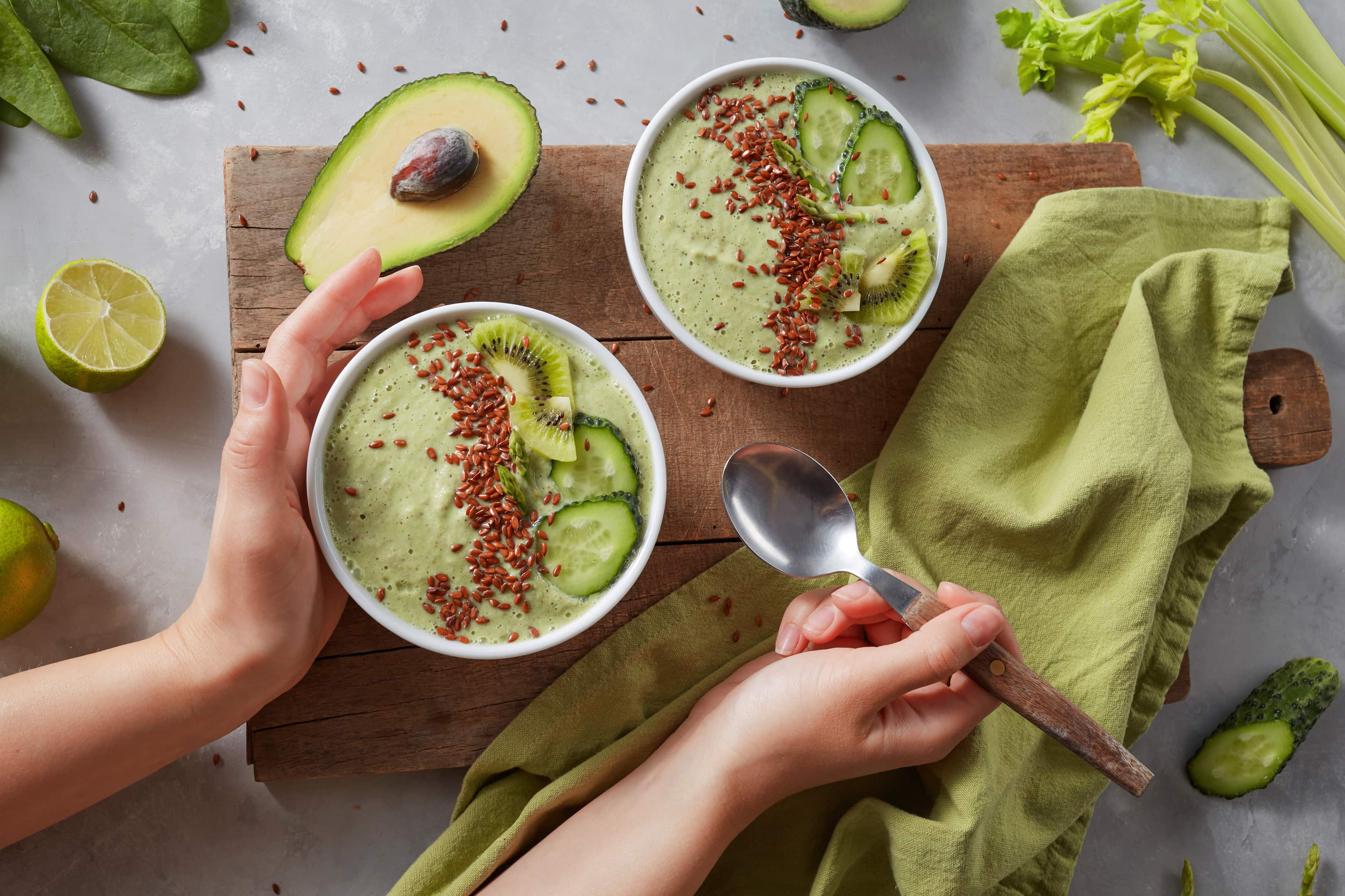 Green smoothie in bowls with fresh kiwi flaxseeds cucumber avocado with female hands