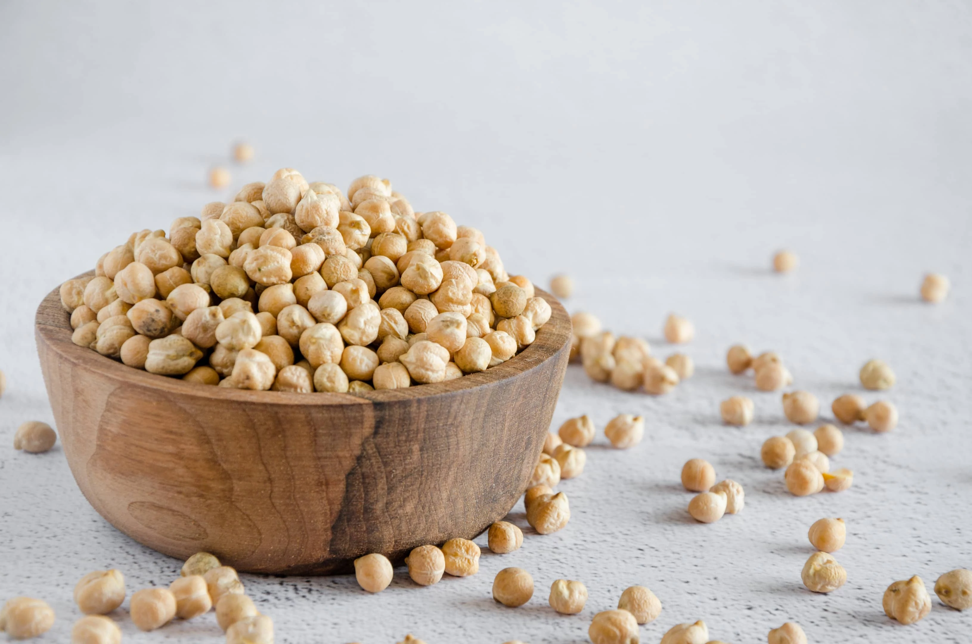 Raw chickpeas in wooden bowl on light surface