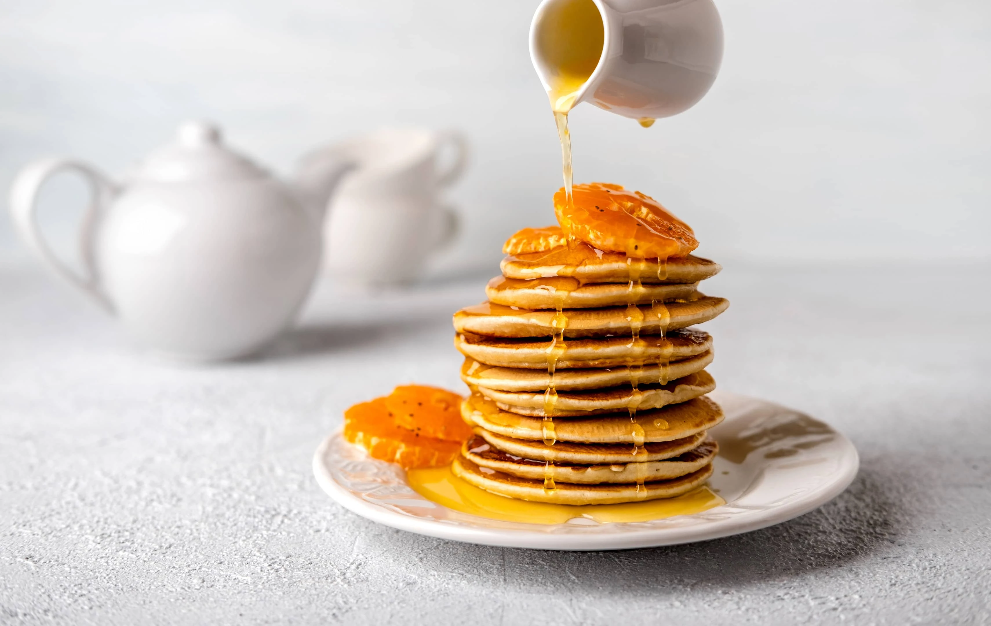 Stack of pancakes with poured maple syrup on light background