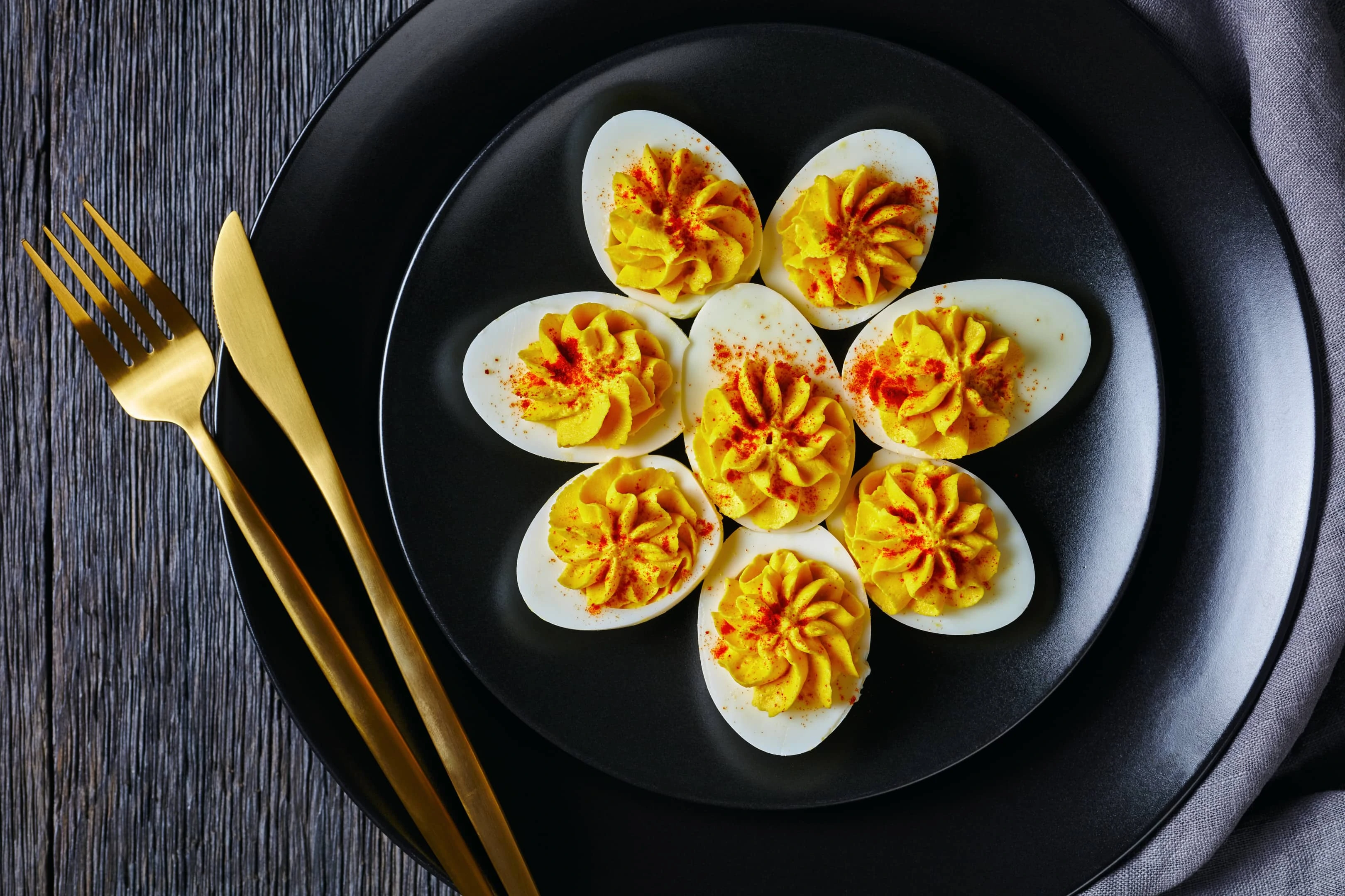 Classic deviled eggs filled with mustard mayonnaise white vinegar sprinkled with smoked paprika on black plate