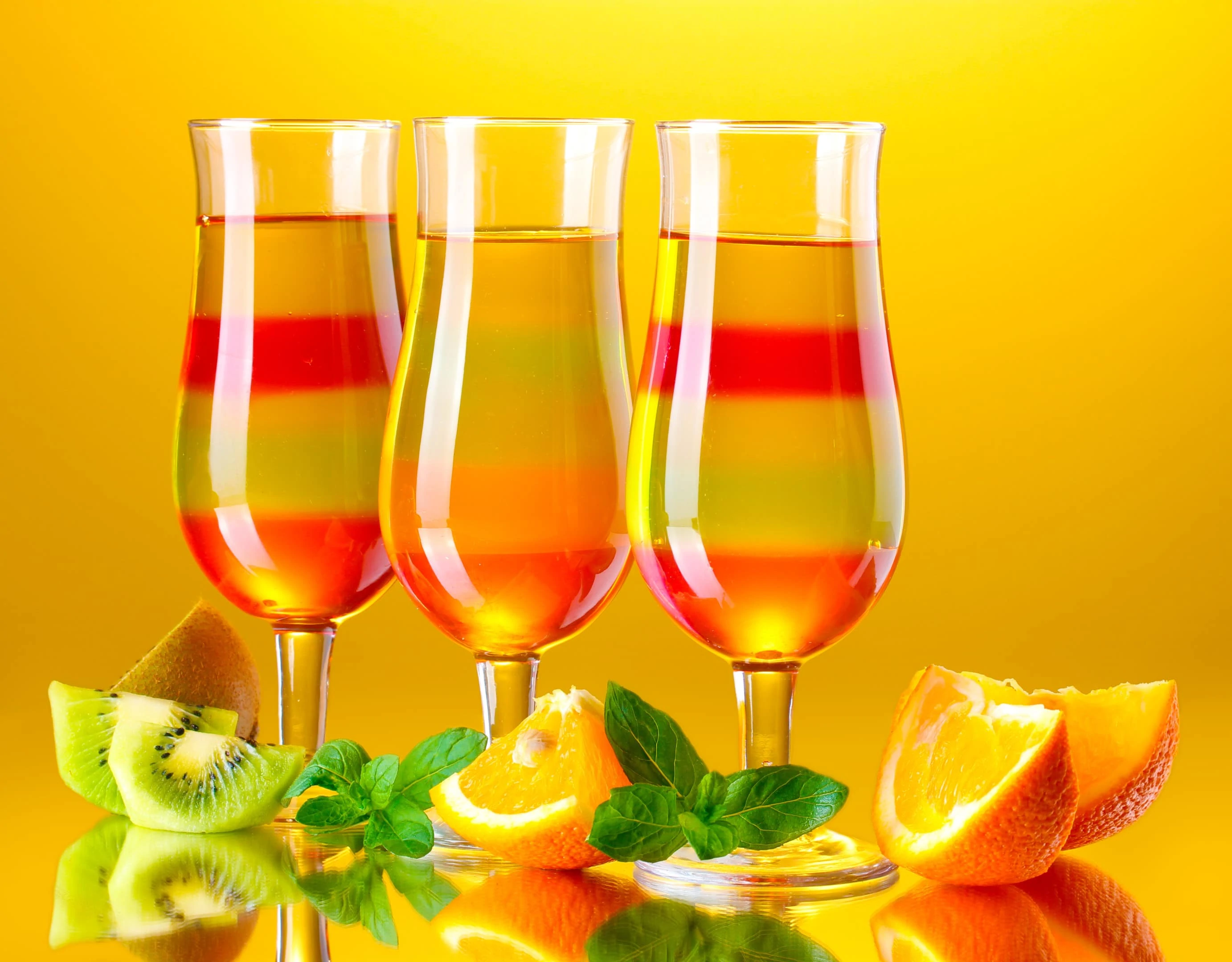 Fruit jelly gelatin in tall glasses with fresh fruits on yellow background
