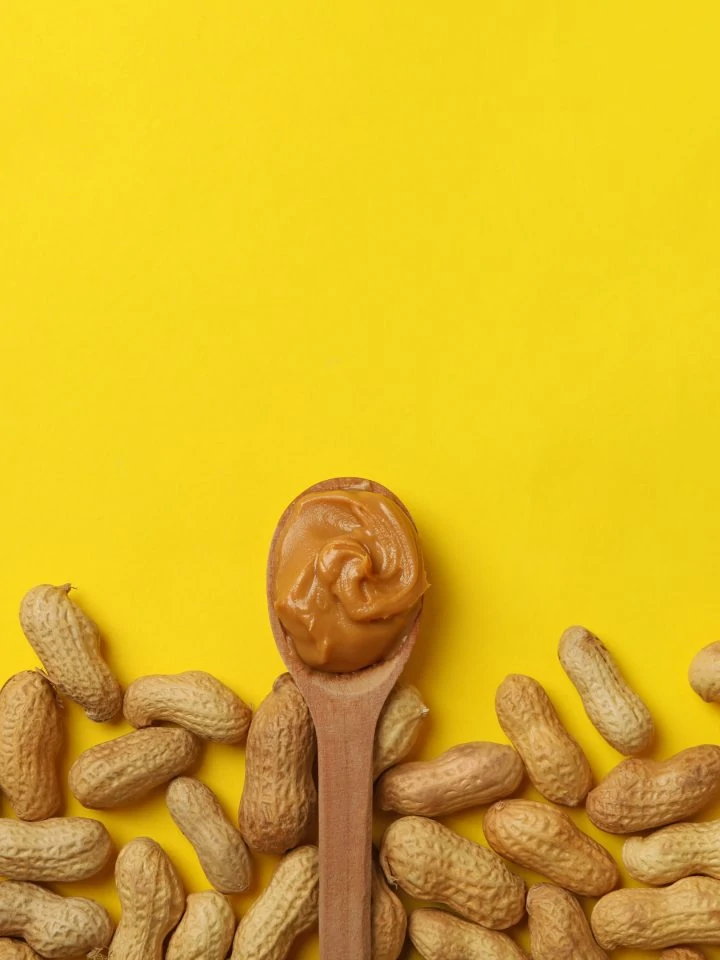 Peanut and spoon with peanut butter on yellow table