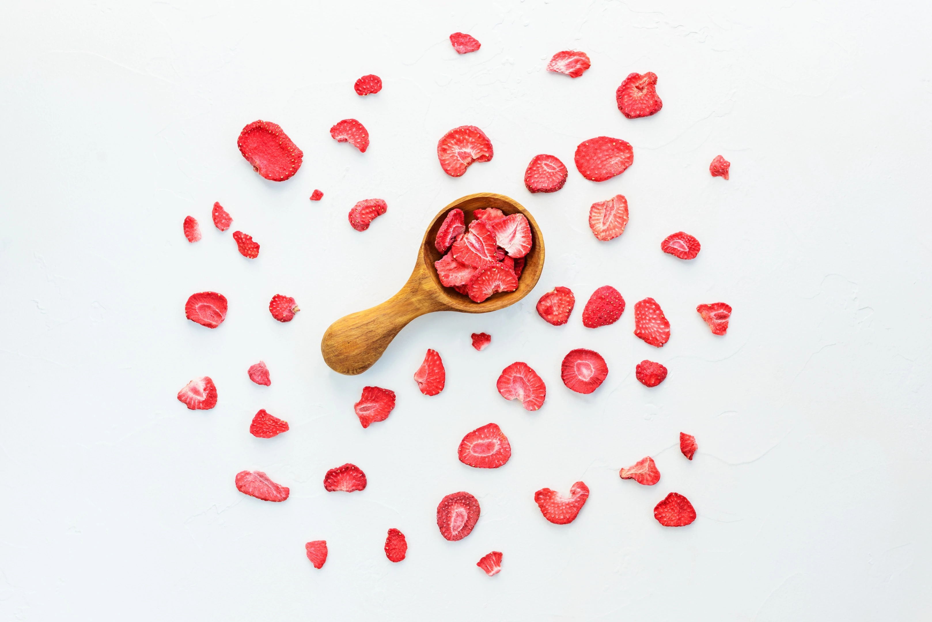 Pieces of dehydrated strawberries with wooden spoon on white background