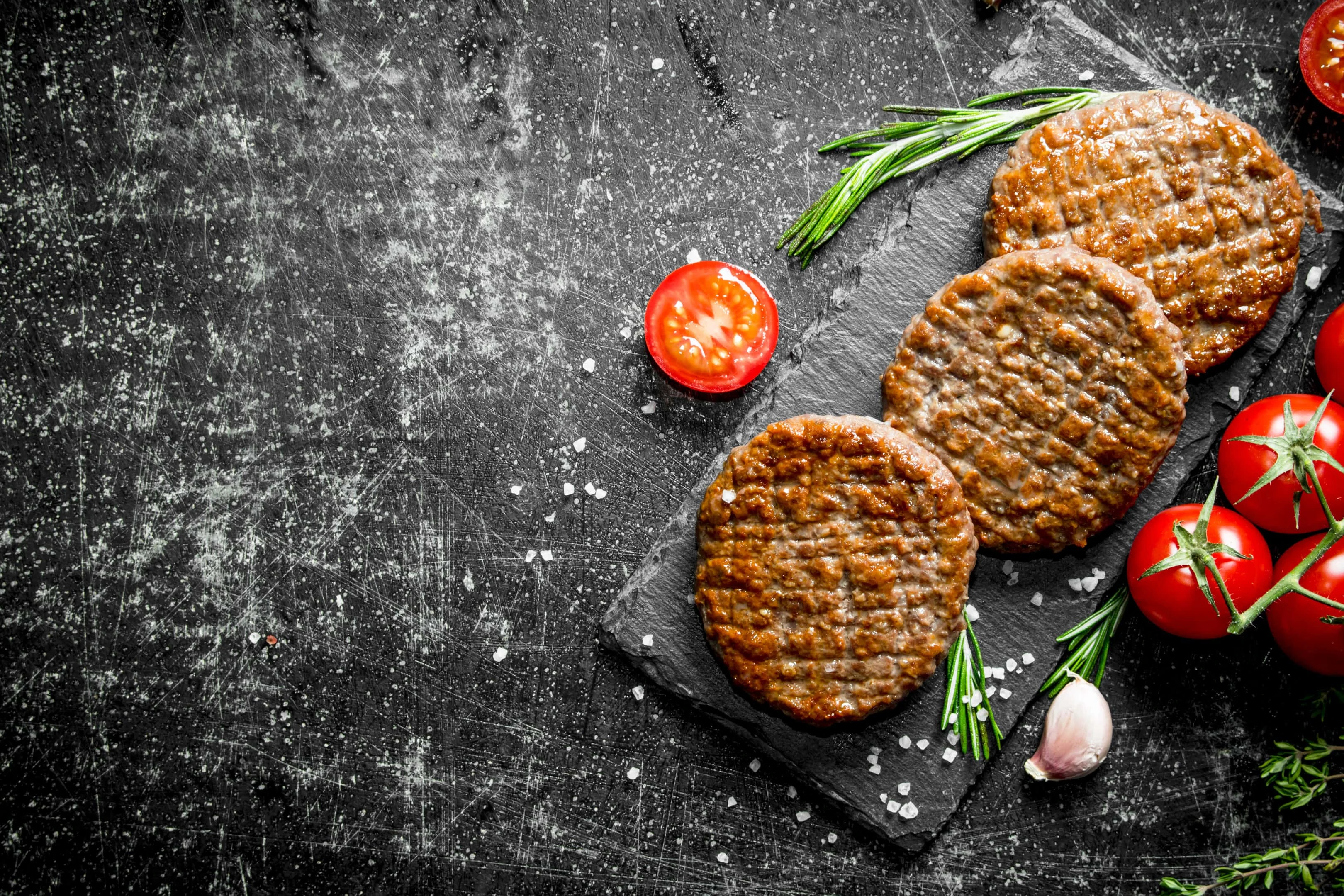 Processed hamburgers with tomatoes on black rustic stone board