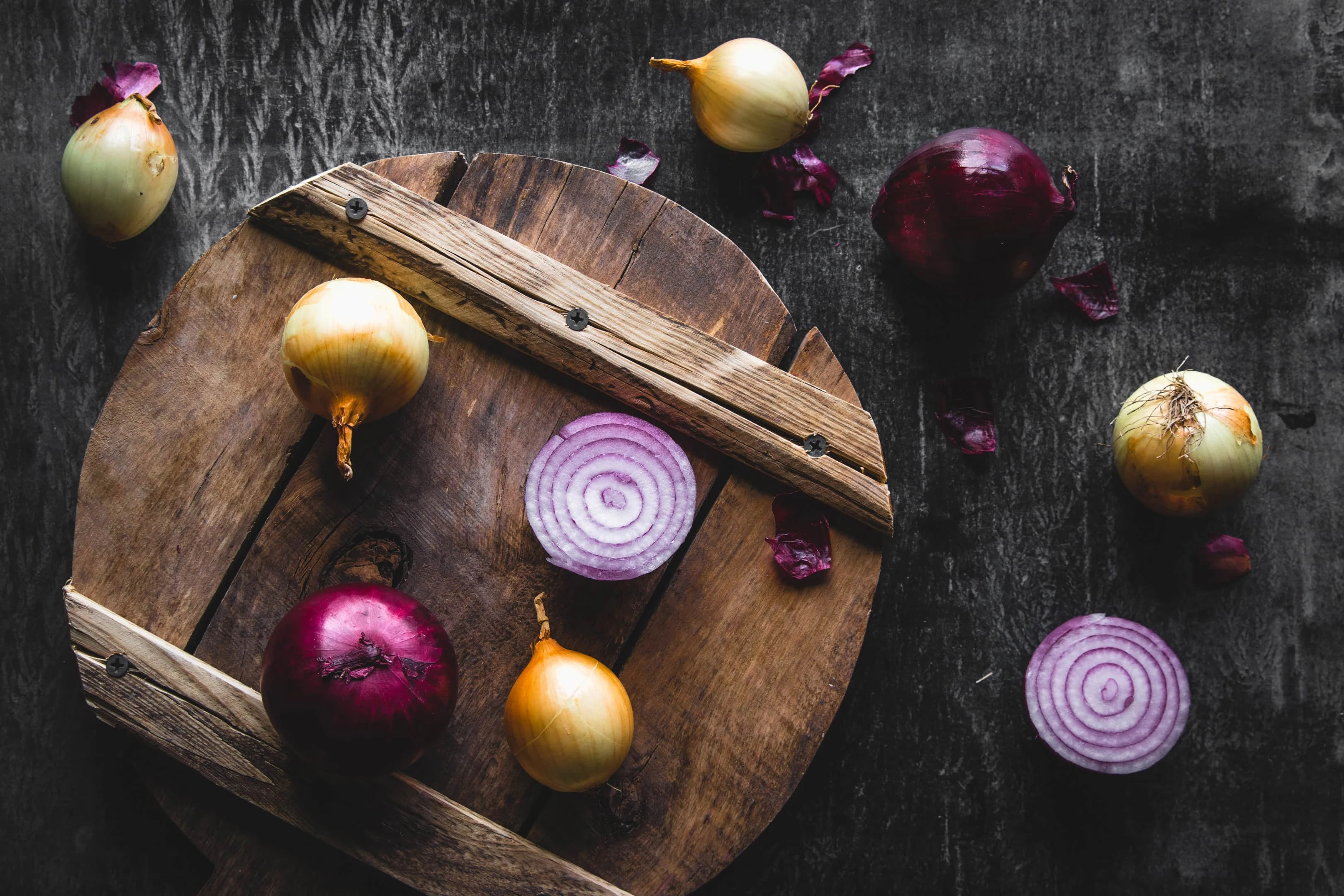 Red onion slices and yellow onions on wooden board