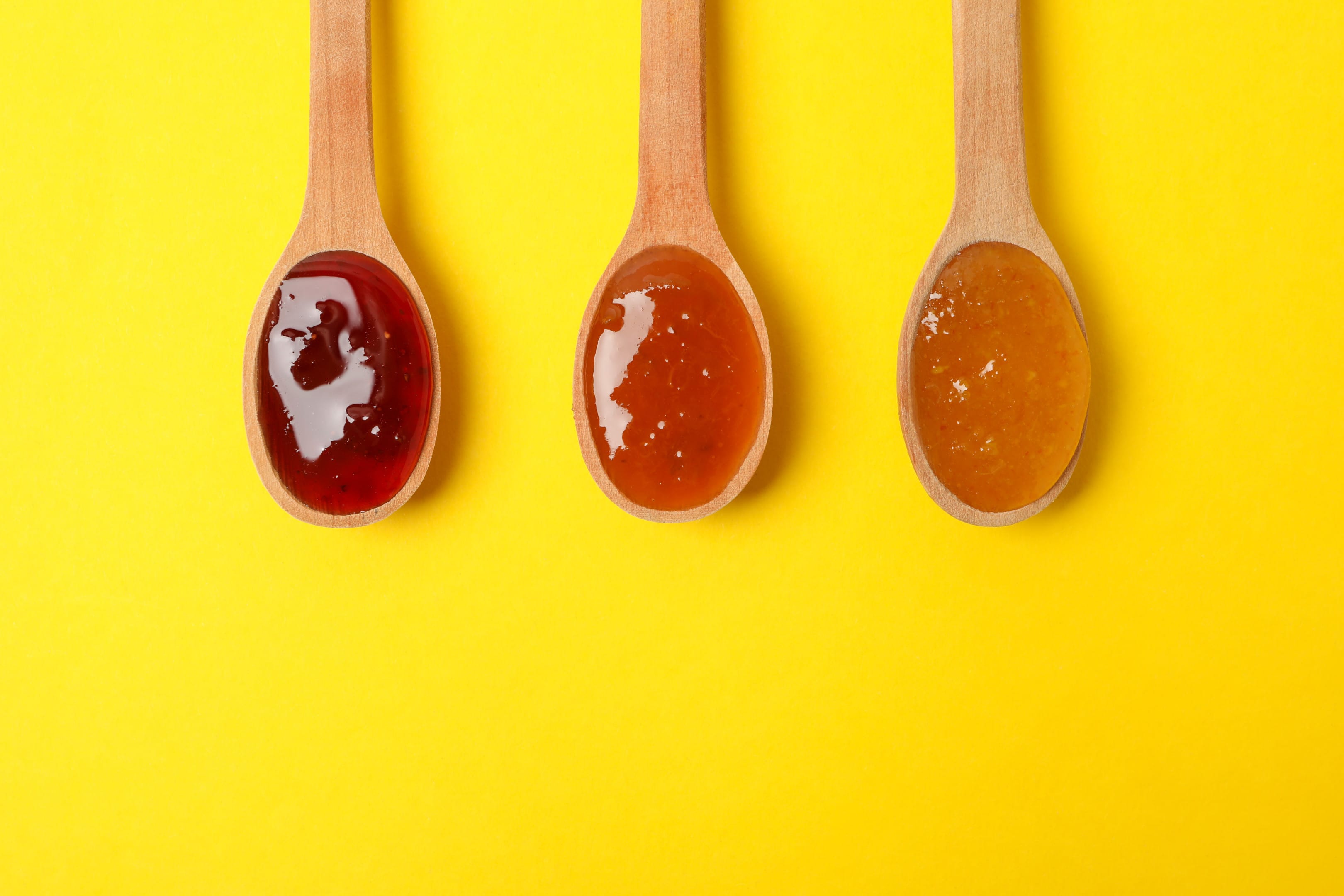 Spoons with jam on yellow background