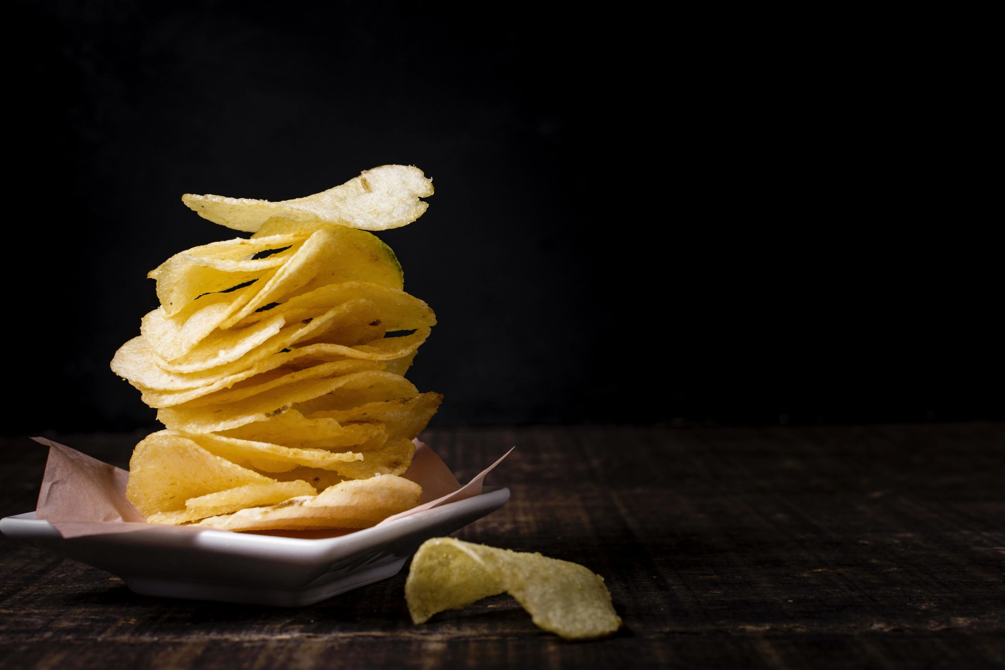 Stacked salty potato chips on black background