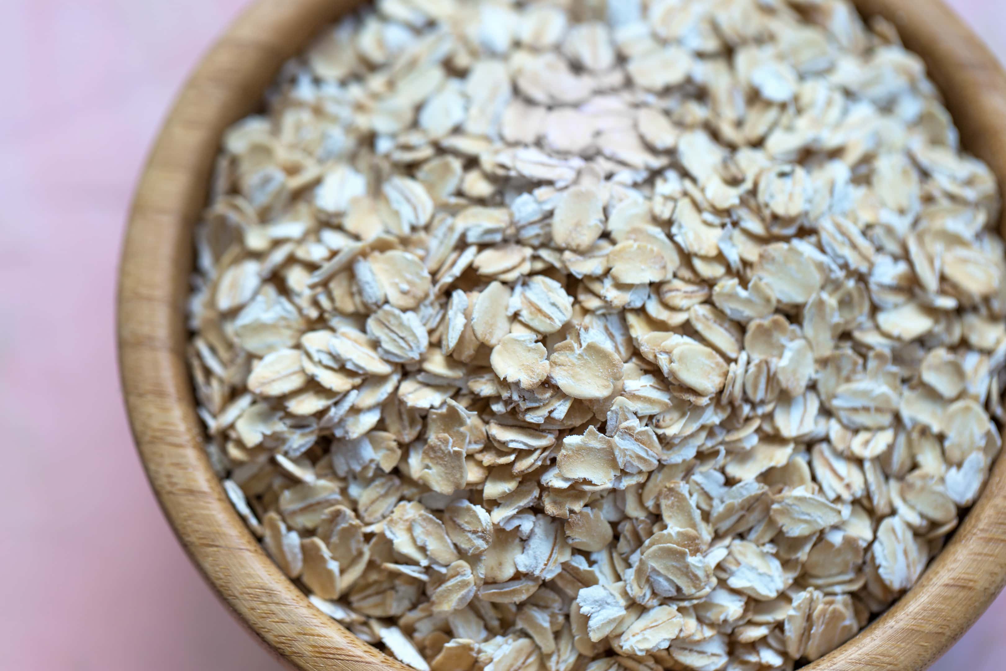 Uncooked rolled oat flakes in wooden bowl