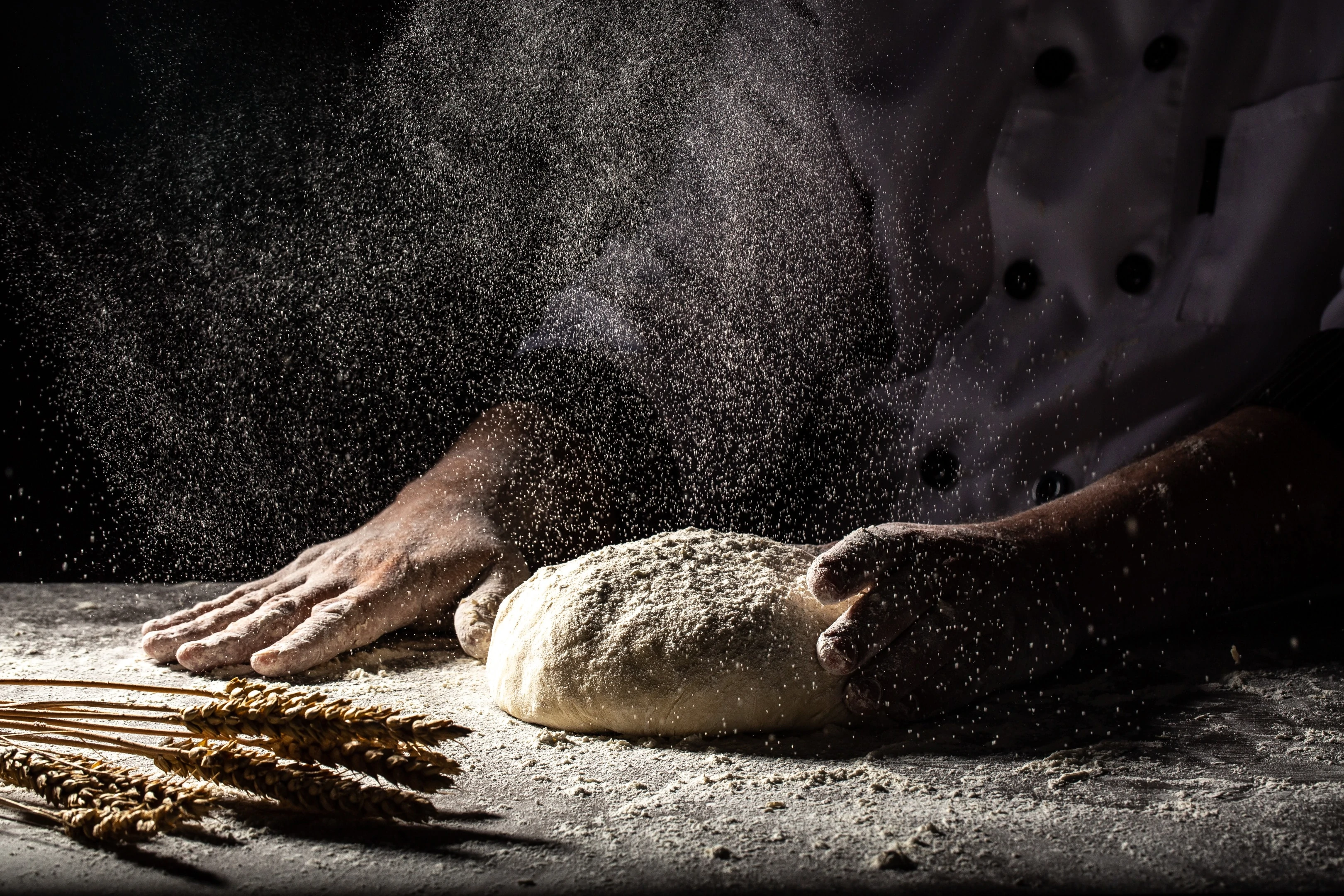 White flour flying into air as pastry chef slams ball of dough with white flour