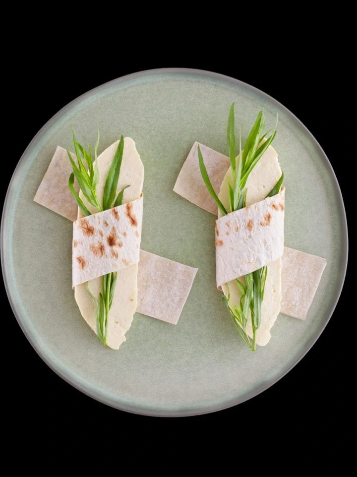 Wrapped pita bread with homemade cheese and tarragon semi dry leaves on round plate