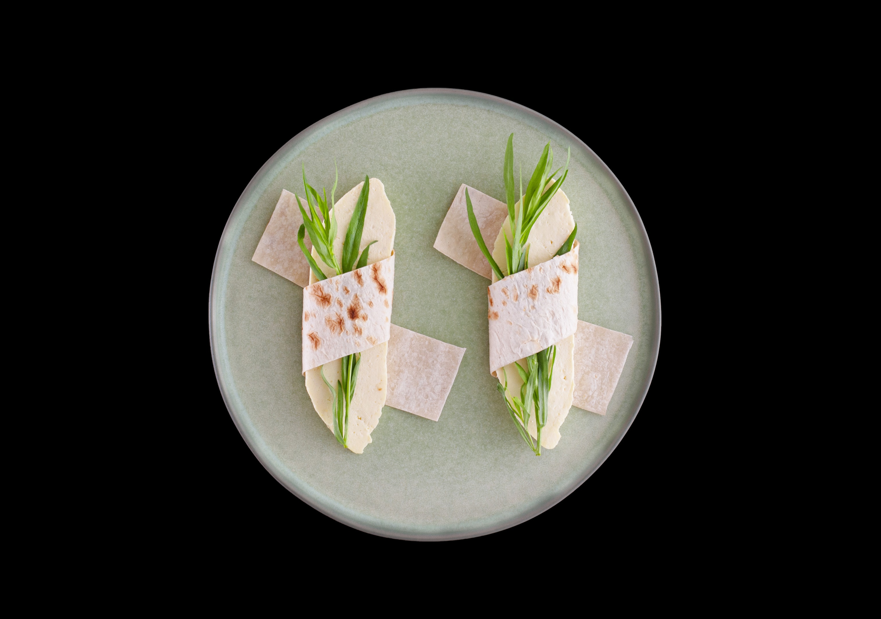 Wrapped pita bread with homemade cheese and semi-dry tarragon leaves on round plate