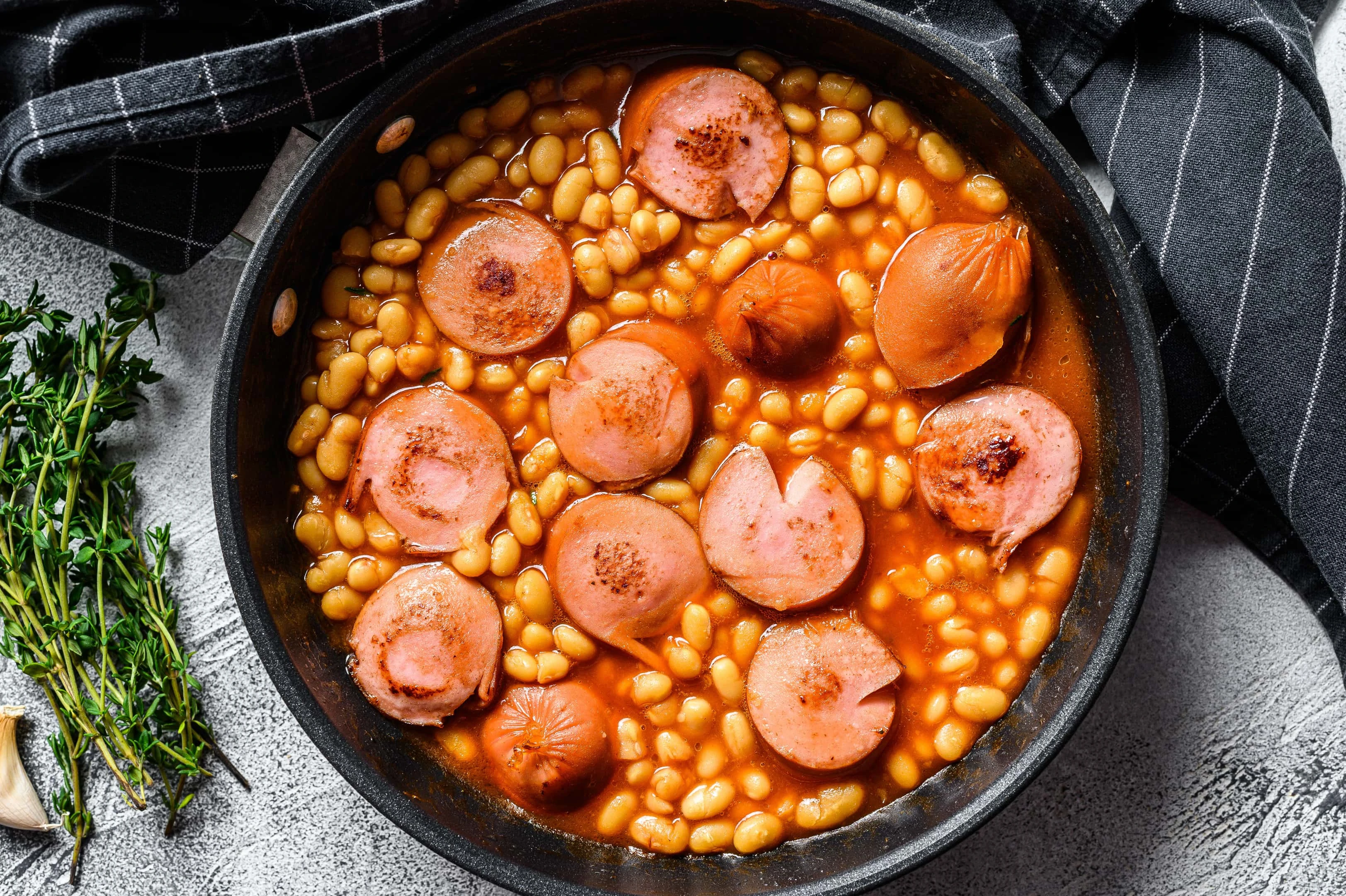 Navy beans with sausages in tomato sauce in a pan. Navy beans are on our list of foods that are high in lysine.