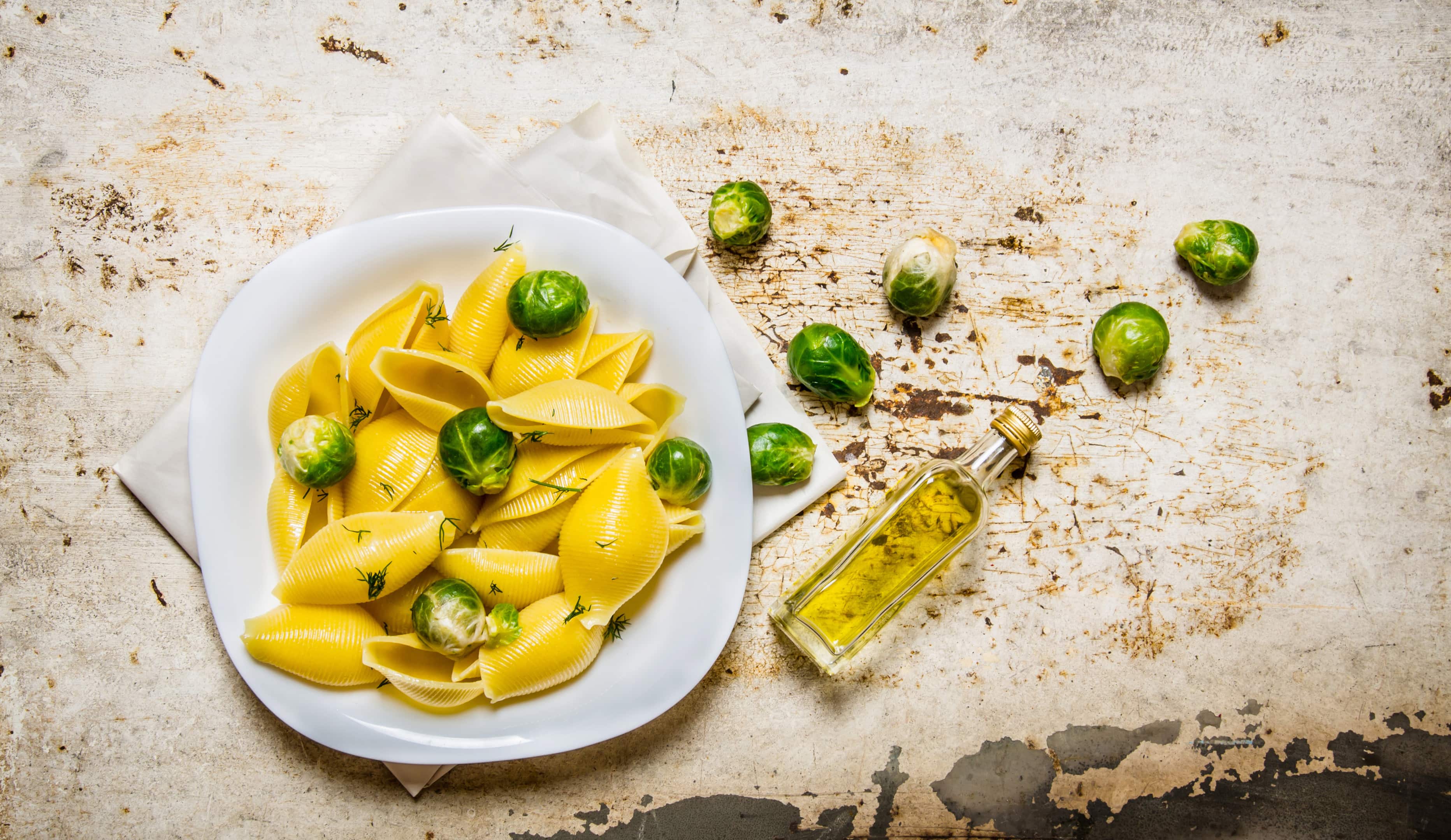 Cooked pasta with brussels sprouts on white plate with olive oil on rustic table