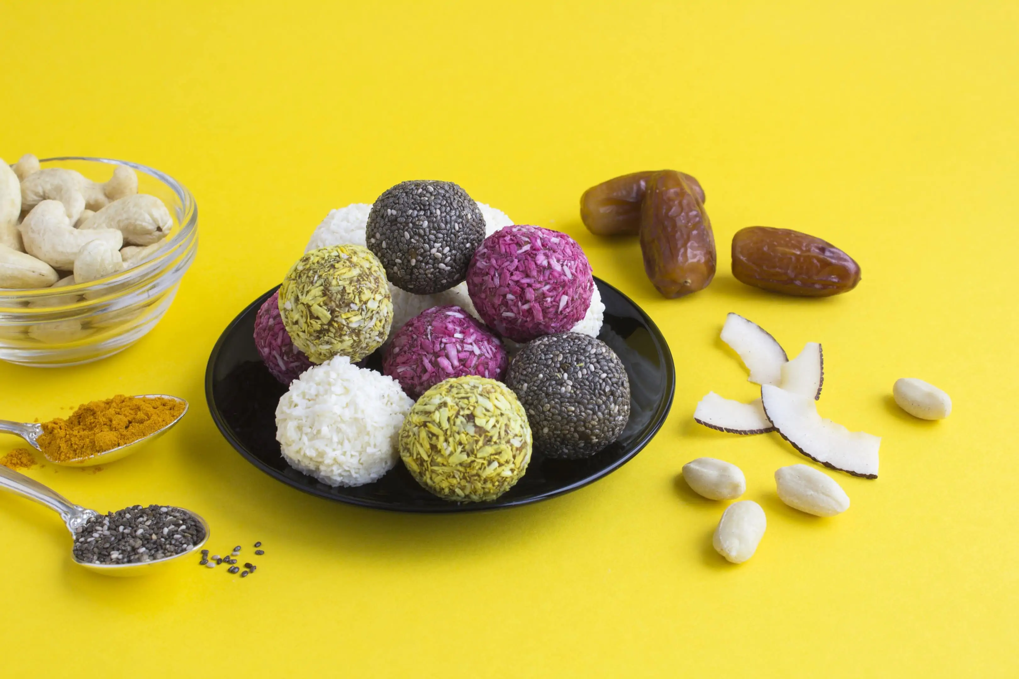 Energy balls of seeds and nuts on black plate on yellow background