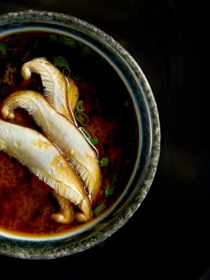 Japanese miso soup with onions seaweed and eryngii mushrooms served in black bowl