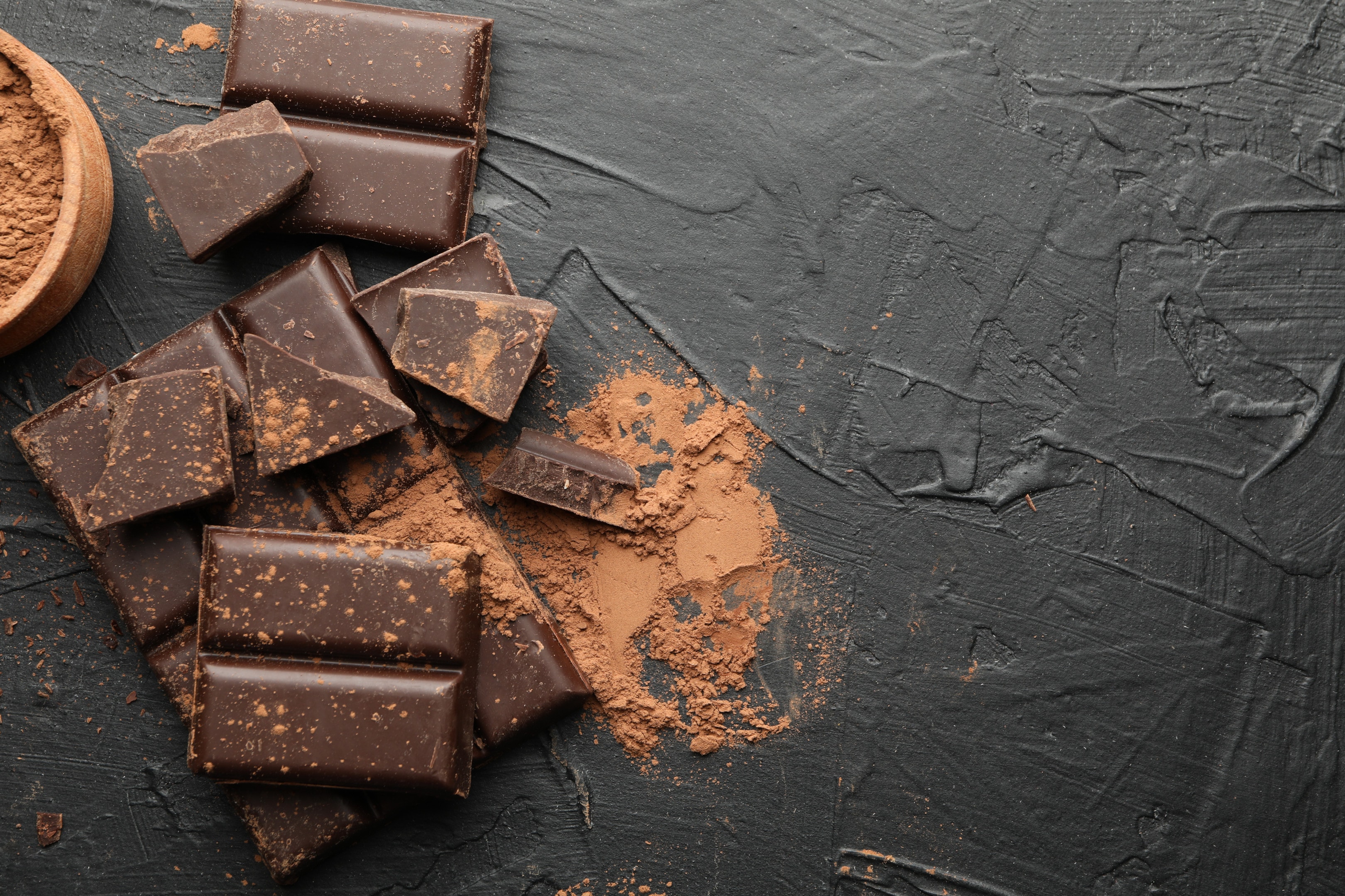 Dark chocolate with cocoa powder on a black concrete table