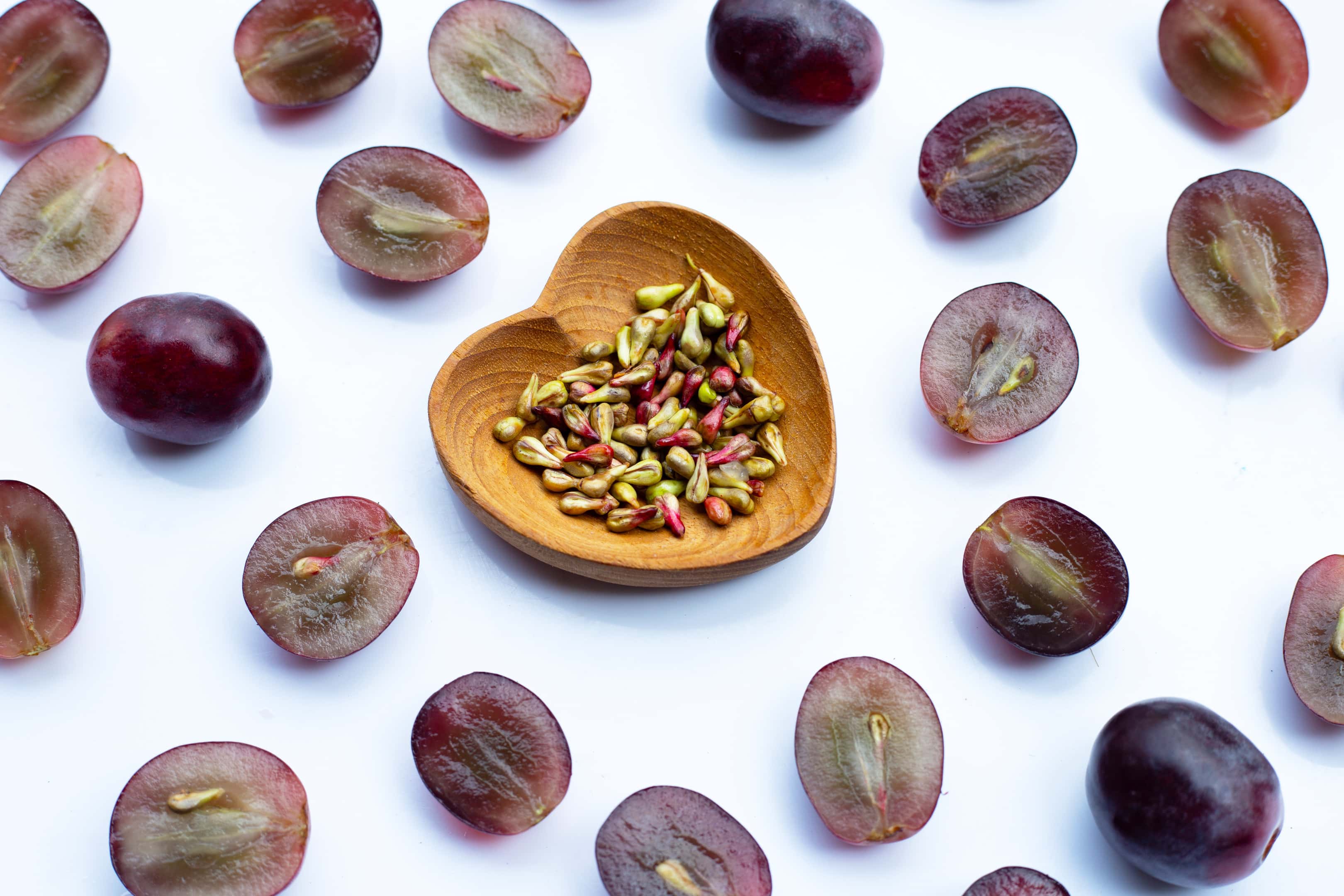 Fresh grapes with grape seeds on white surface