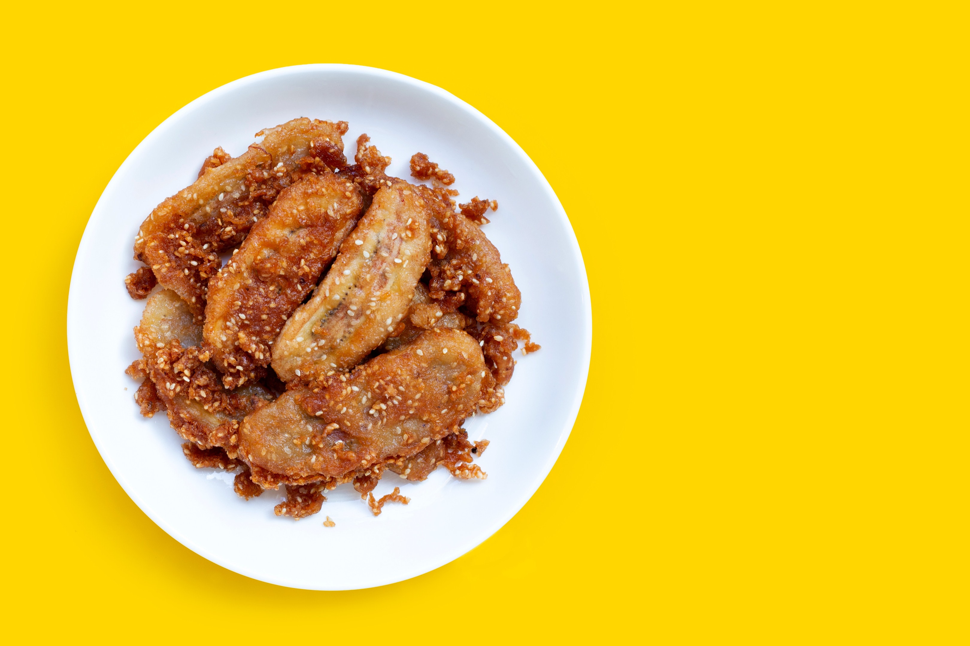 Fried bananas with sesame seeds on yellow background