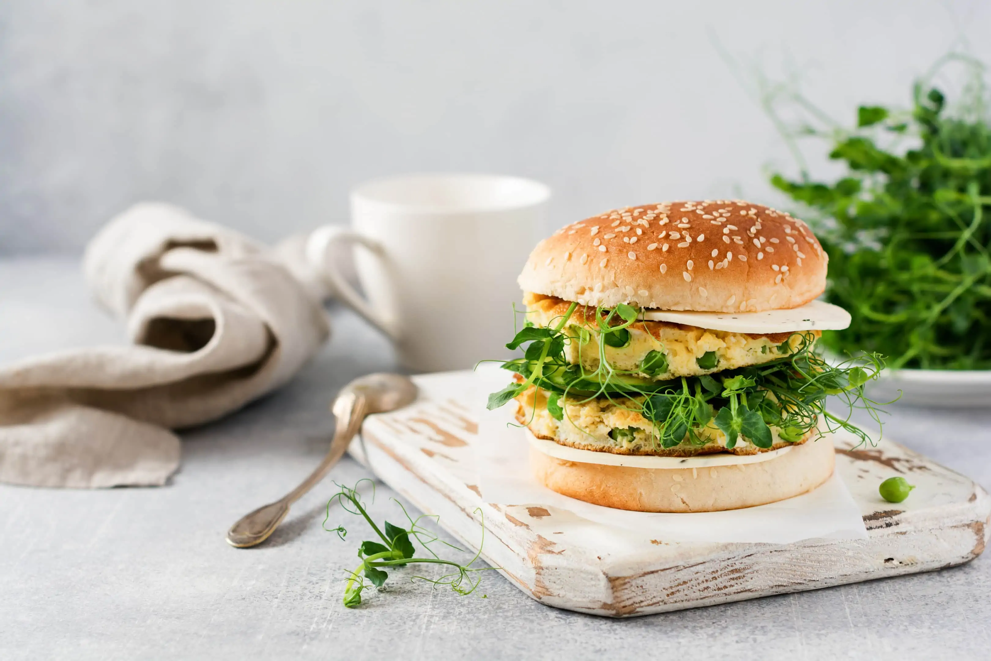 Vegetarian burger with egg and pea shoots on wooden cutting board