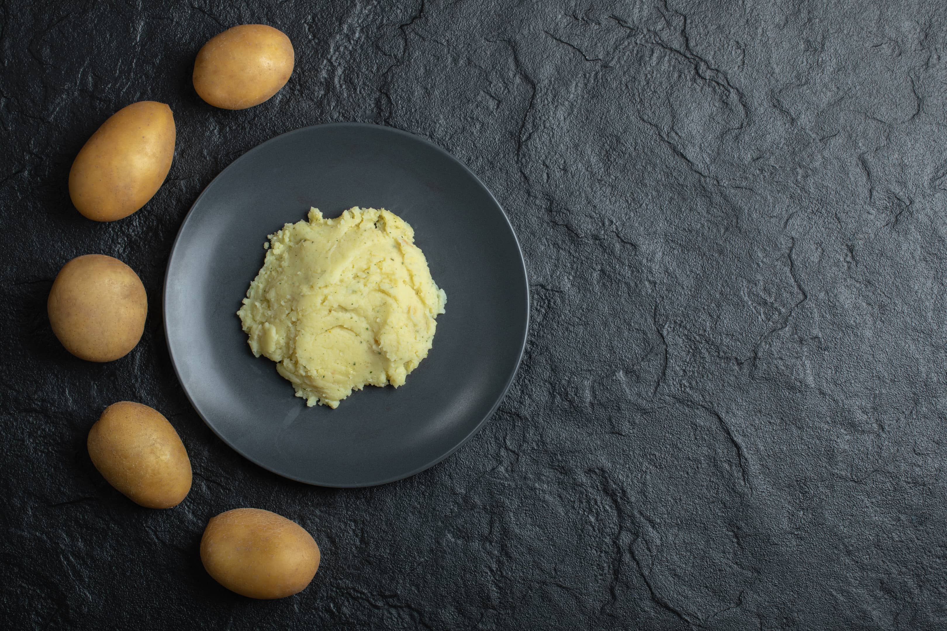 Fresh potatoes and mashed potatoes on black table