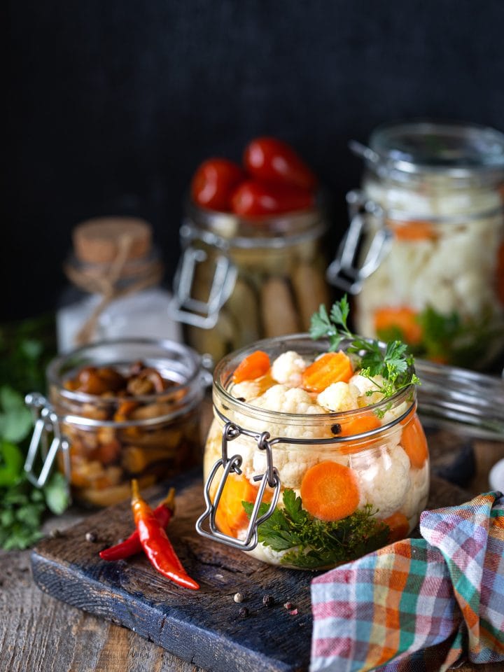 Fermented cauliflower with carrots in a glass jar on wooden table
