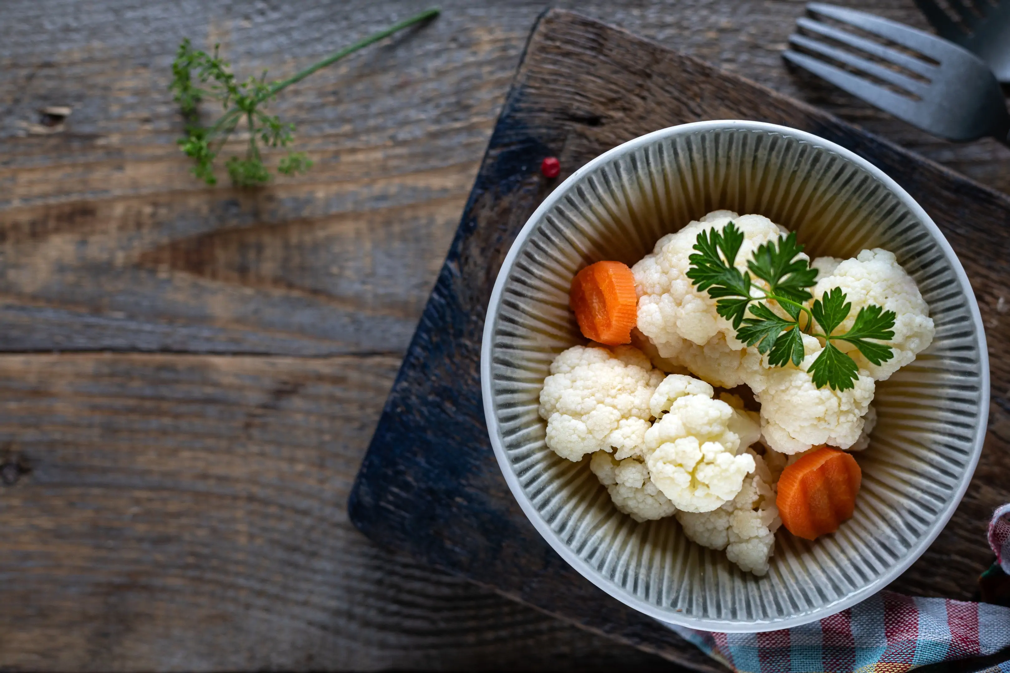 Fermented cauliflower with carrots in a ceramic plate on wooden table - top view
