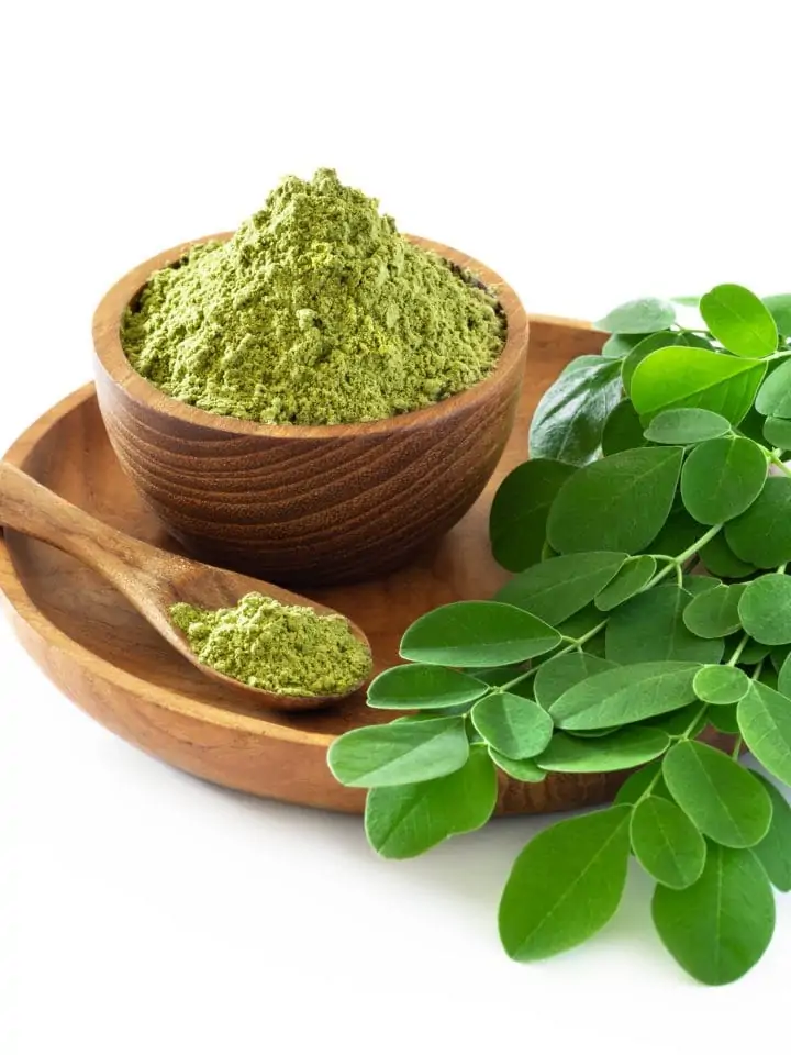 Moringa powder in wooden bowl with fresh moringa leaves