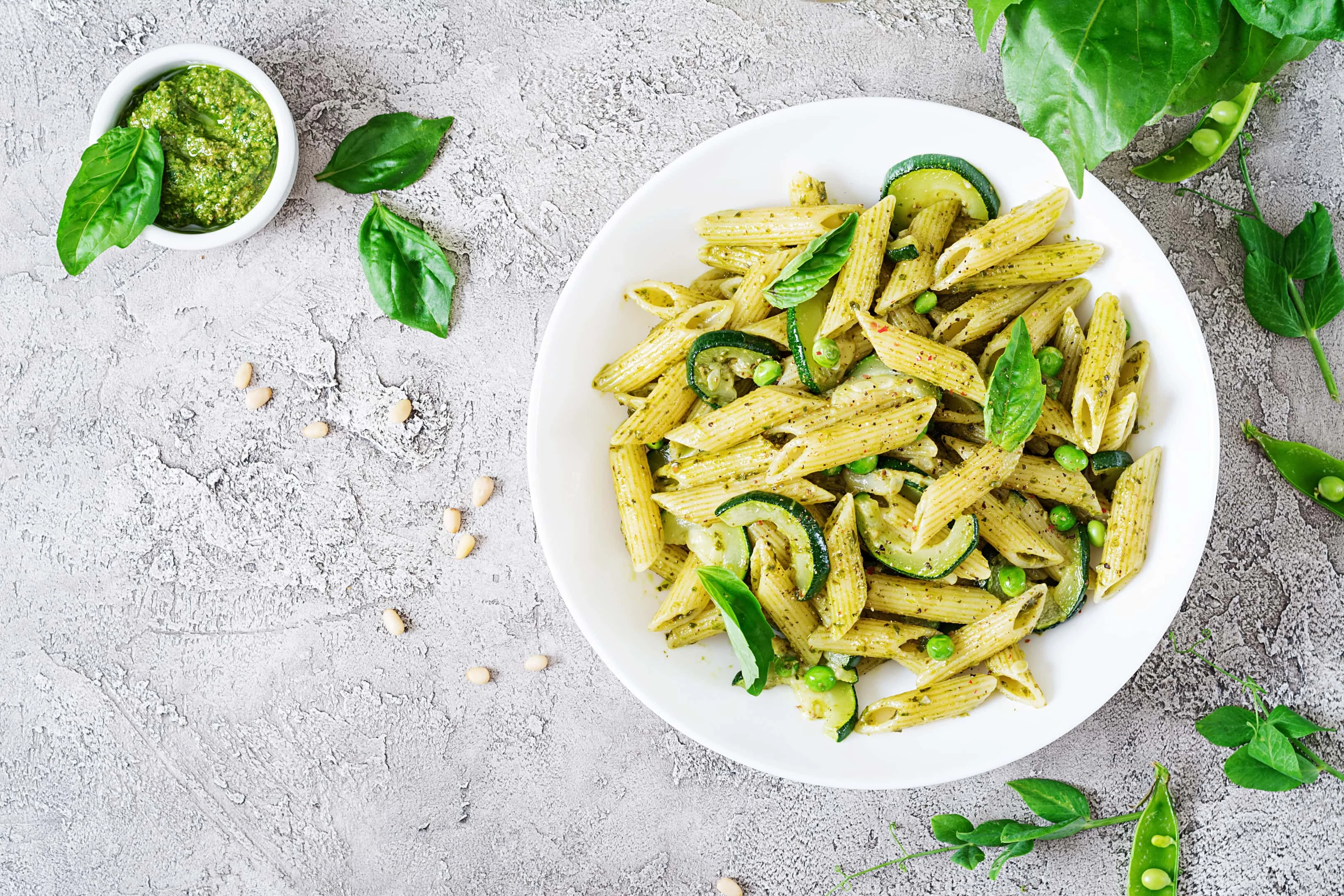 Penne pasta with pesto sauce, zucchini, green peas and basil