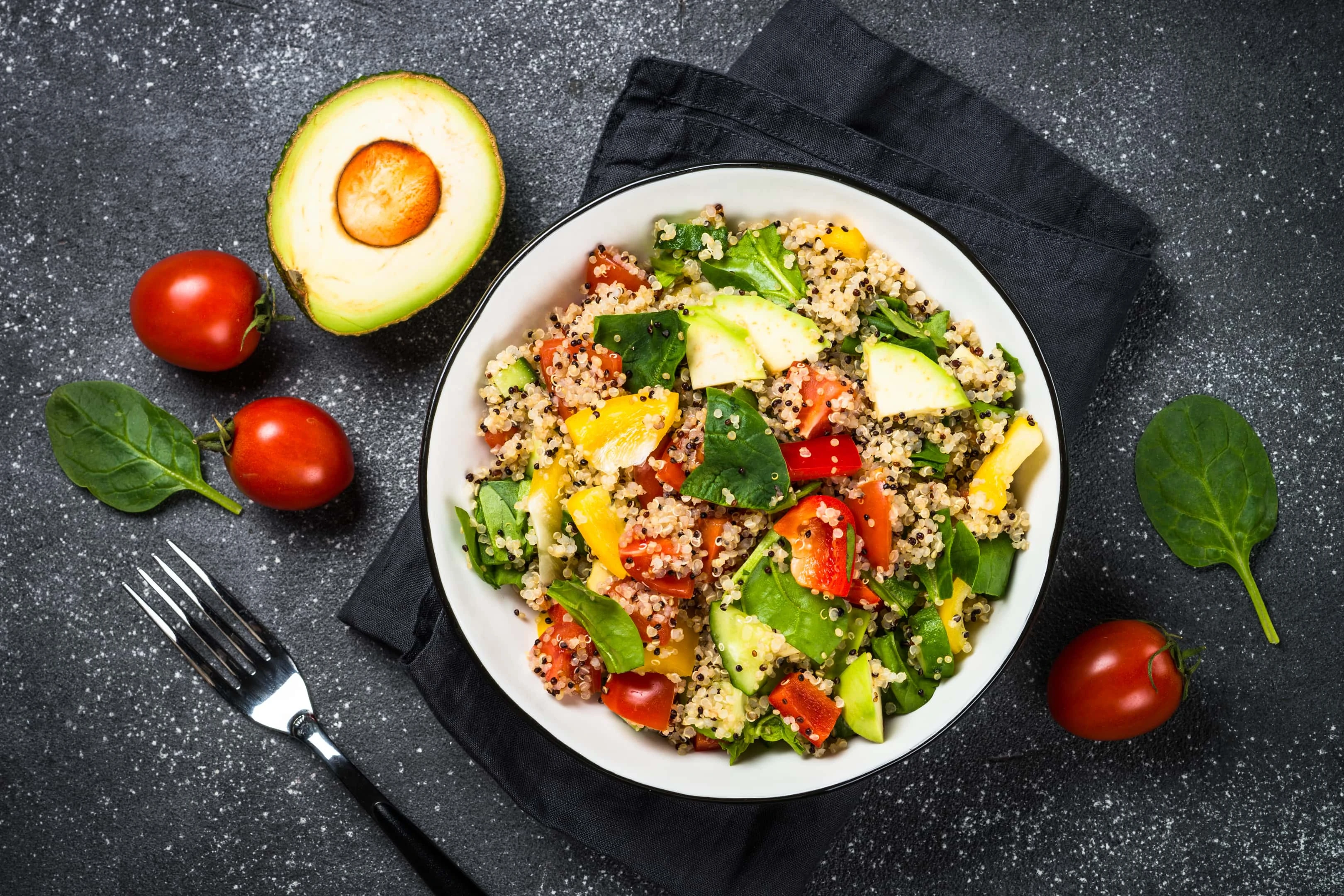 Quinoa salad with spinach, avocado, paprika and tomatoes on black stone table