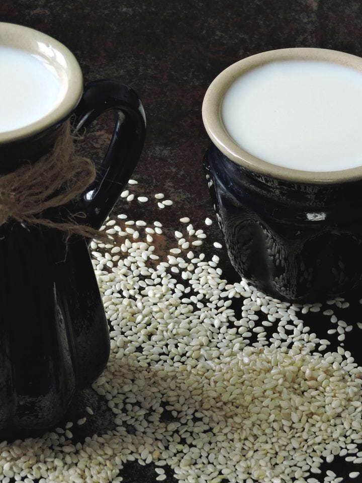 Sesame milk in jug and mug with scattered sesame seeds