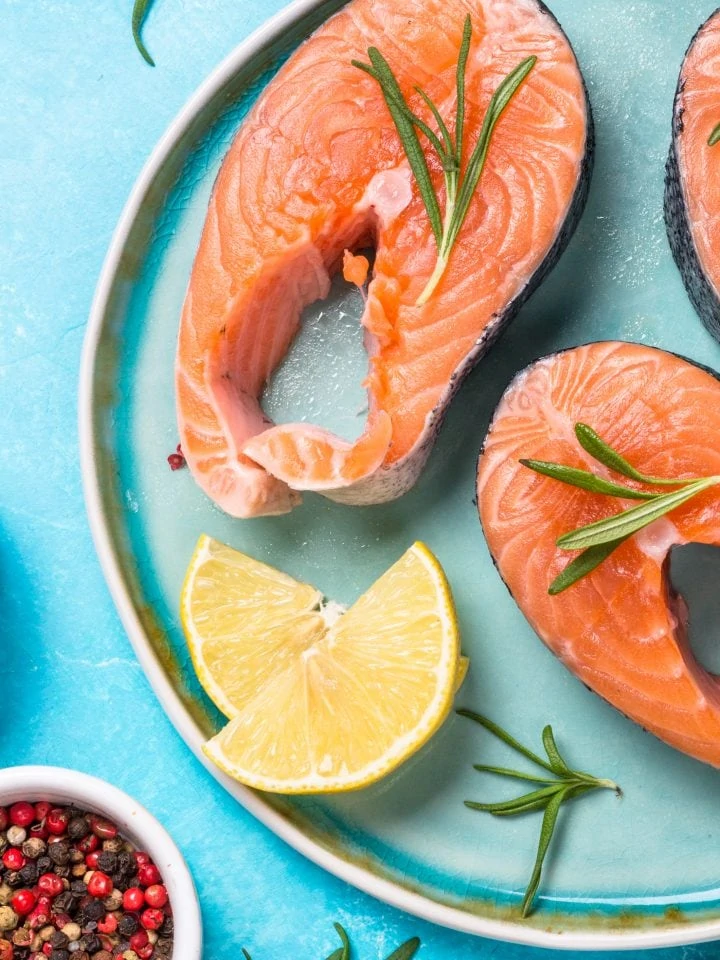 Raw Salmon fish steak on blue plate with ingredients for cooking