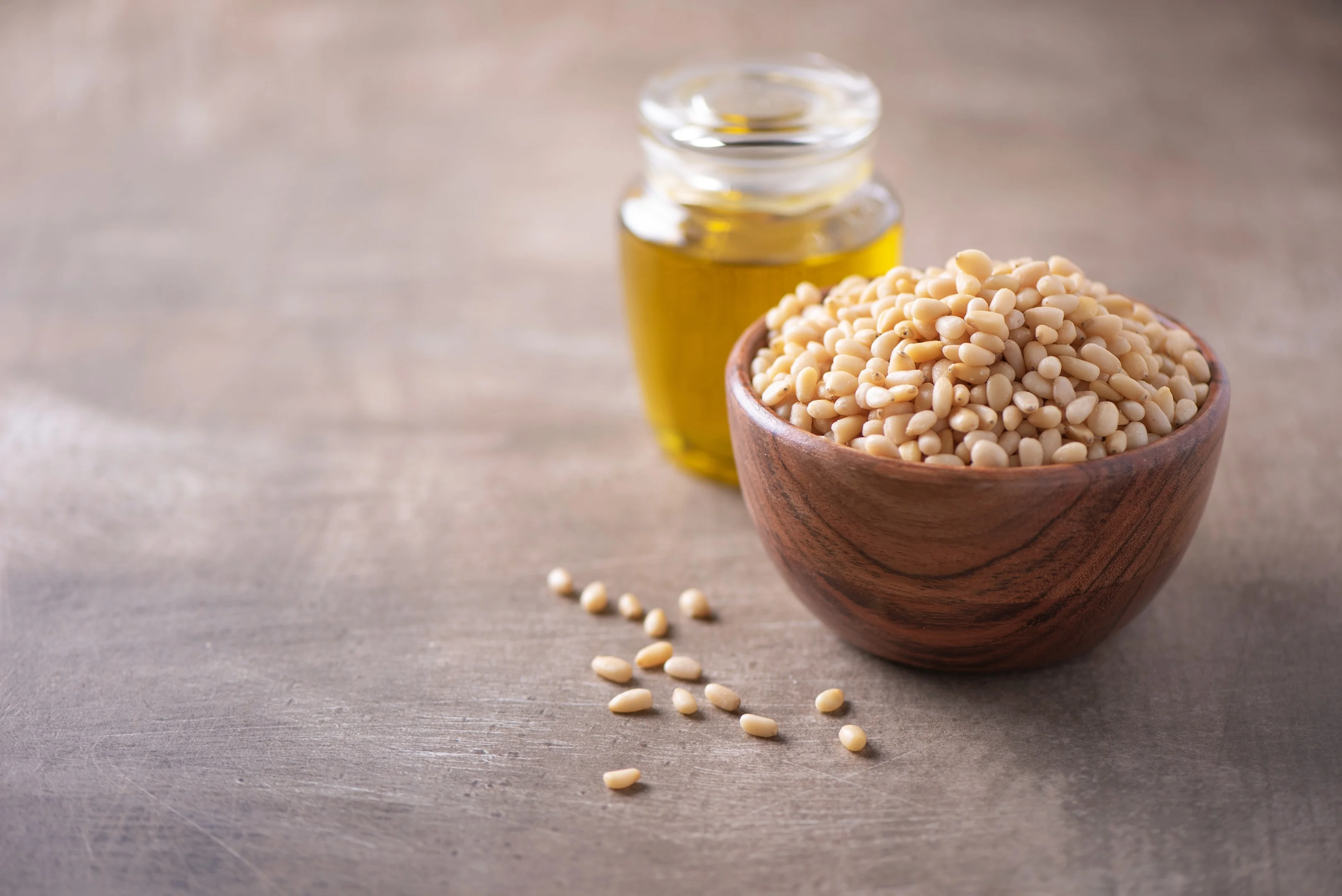 Shelled raw pine nuts in wooden bowl and pine nuts oil