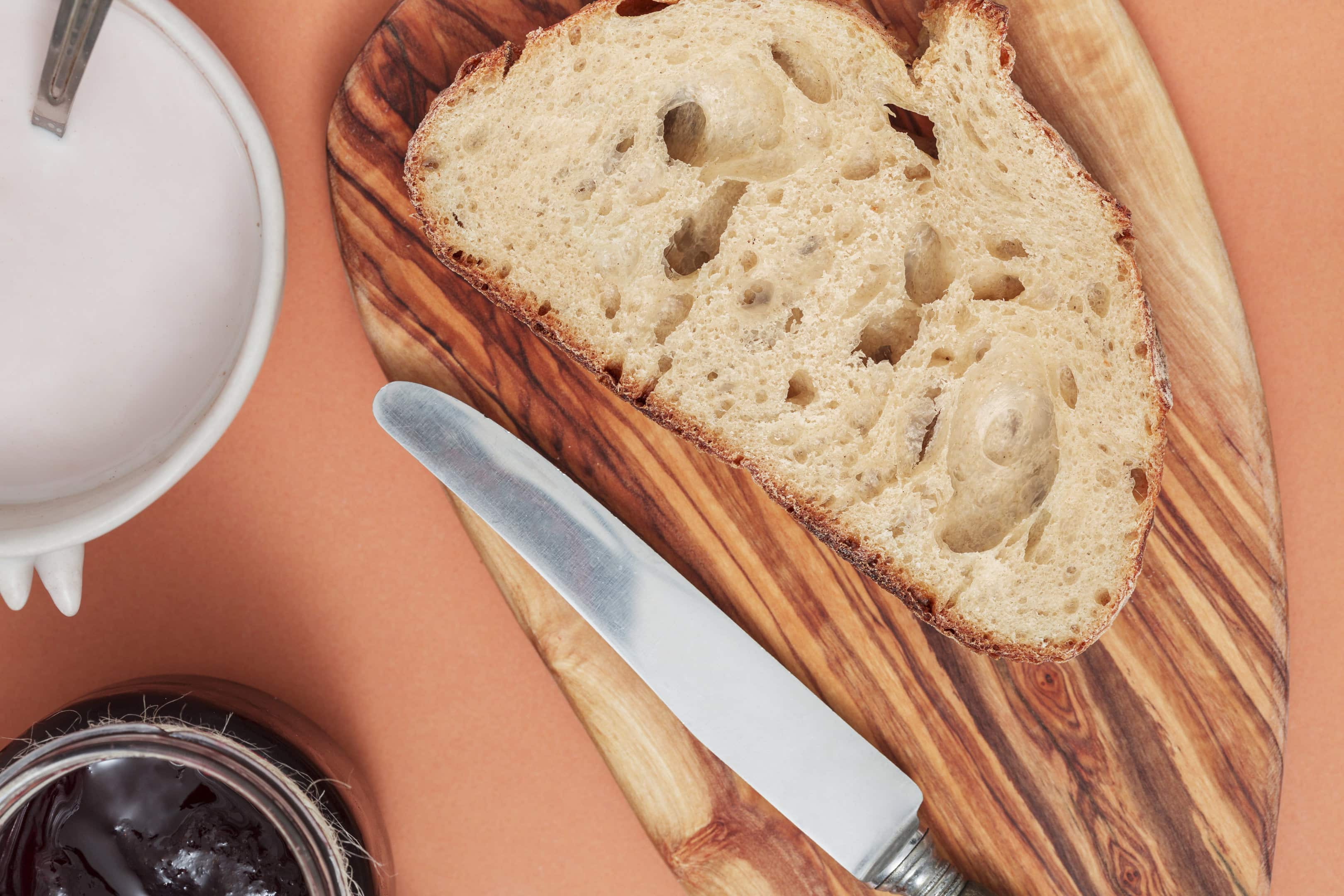 Sliced King Arthur's sourdough bread with a knife, chopping board, milk, and jam