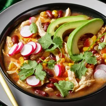 Flavorful chicken tortilla soup Pioneer Woman with tomato, corn, red kidney beans, avocado, radish, lime, chile and fresh cilantro