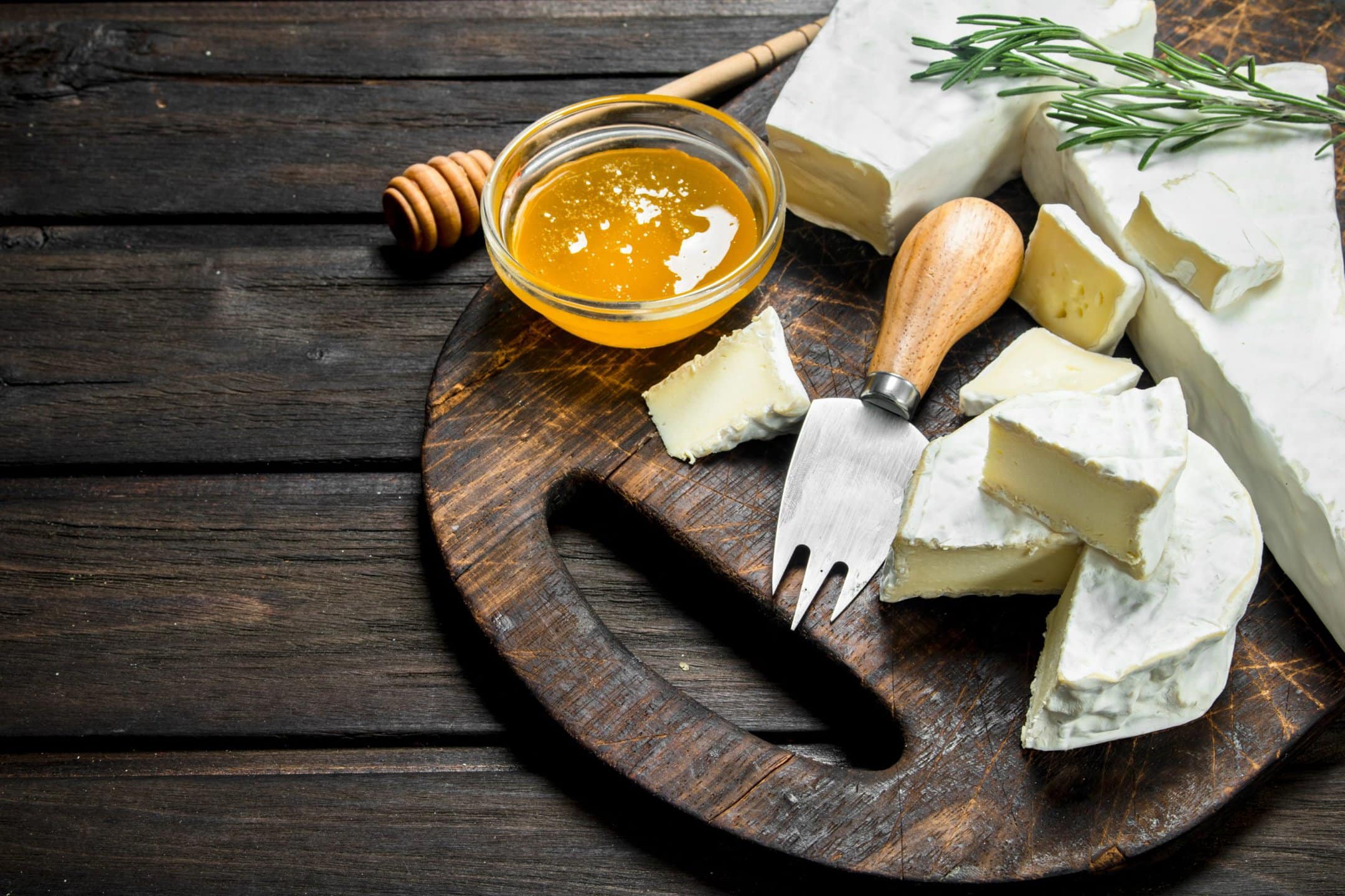 Brie cheese with honey and rosemary on a cutting board.